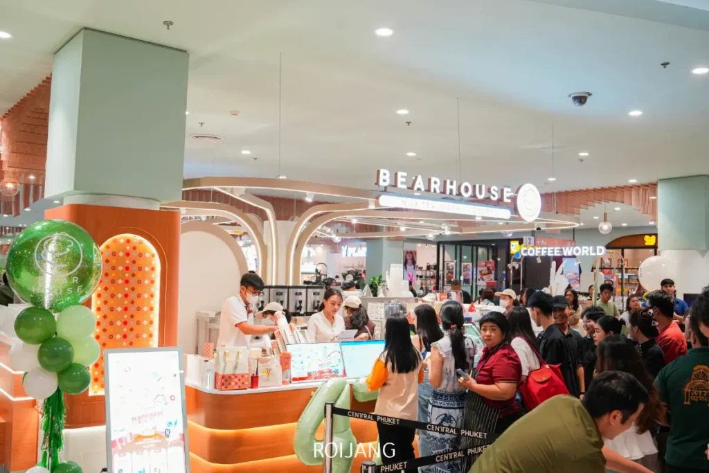 ผู้คนจำนวนมากยืนรอคิวที่เคาน์เตอร์ BEARHOUSE ภายในห้างสรรพสินค้า โดยมีพนักงานให้บริการลูกค้าและร้านค้าอื่นๆ มองเห็นได้ในพื้นหลัง.