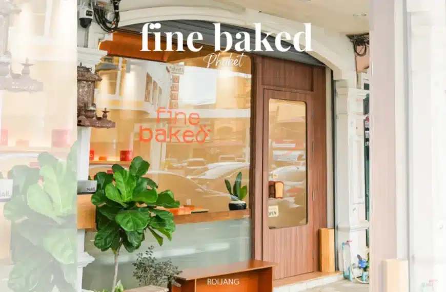 มุมมองถนนของร้านเบเกอรี่ BEARHOUSE ที่มีประตูไม้ หน้าต่างบานใหญ่แสดงคำว่า "Fine Baked" พืชสีเขียวอยู่ด้านนอก และหน้าร้านที่สว่างสดใสและเชิญชวน.