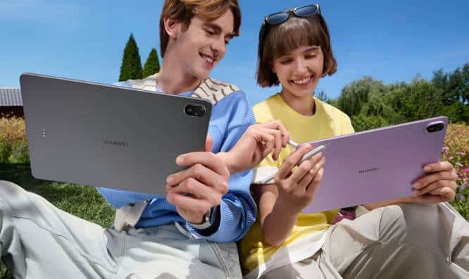 สองคนนั่งอยู่กลางแจ้ง ยิ้มและใช้สไตลัสกับแท็บเล็ต Huawei.