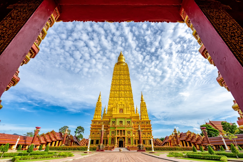 วัดทองคำสูงใหญ่ประดับประดาอย่างวิจิตรตระการตาพร้อมรายละเอียดที่ซับซ้อนตั้งอยู่ใต้ท้องฟ้าที่มีเมฆบางส่วนปกคลุม ล้อมรอบด้วยซุ้มประตูประดับสีแดงและทอง—หนึ่งในสถานที่ที่ต้องไปเยือนสำหรับผู้ที่มองหา ที่เที่ยวกระบี่.