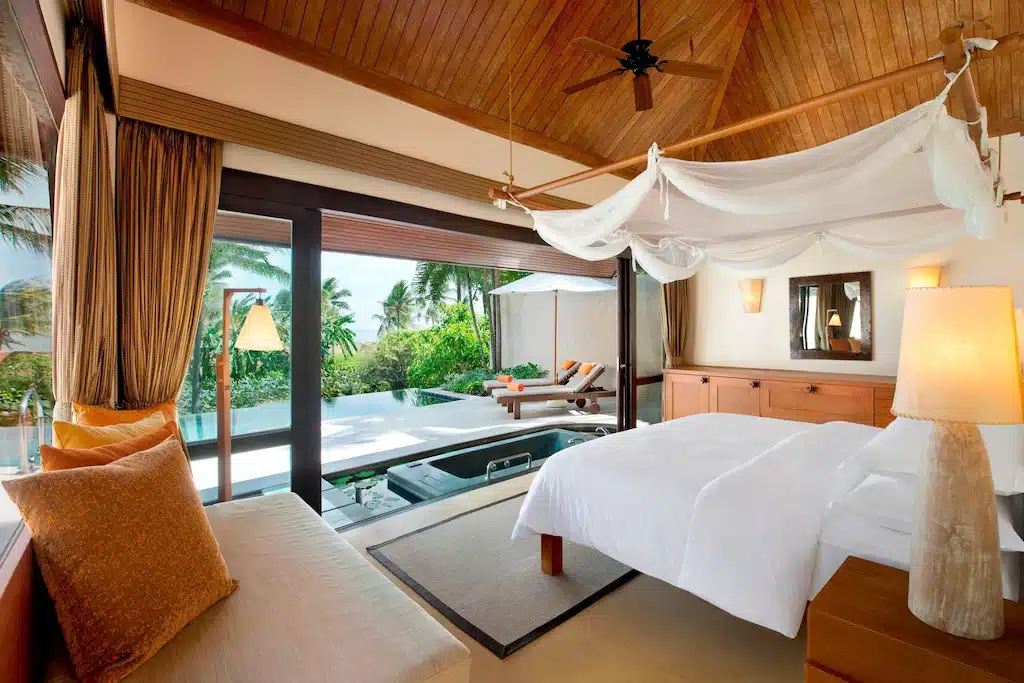 ที่พักปราณบุรีติดทะเลสไตล์โมเดิร์นเป็นหลัง พร้อมเตียงผ้าใบ, เพดานไม้, หน้าต่างบานใหญ่, เก้าอี้พักผ่อนบนระเบียง, และสระว่ายน้ำกลางแจ้งขนาดเล็กที่ล้อมรอบด้วยต้นไม้เขียวชอุ่มเพื่อการพักผ่อนอย่างผ่อนคลาย.
