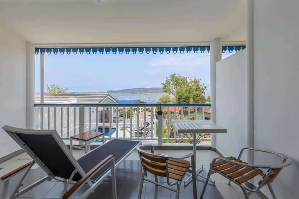 ระเบียงที่มีหลังคาคลุม พร้อมเก้าอี้เลานจ์ โต๊ะเล็ก และเก้าอี้สองตัว รวม ที่เที่ยวเกาะสีชัง เกาะสวยๆ ในที่เที่ยวชลบุรี ไป เที่ยวเกาะสีชัง เดินทางง่ายๆ ใกล้กรุงเทพแบบไปเช้าเย็นกลับได้ หลีกหนีความวุ่นวาย พร้อมอวดสถานที่สโลว์ไลฟ์
มองเห็นหลังคาบ้าน ต้นไม้ และวิวทะเลและเกาะที่มีภูเขาไกลๆ—เหมาะสำหรับการพักผ่อนหลังจากวันท่องเที่ยวเกาะสีชัง.