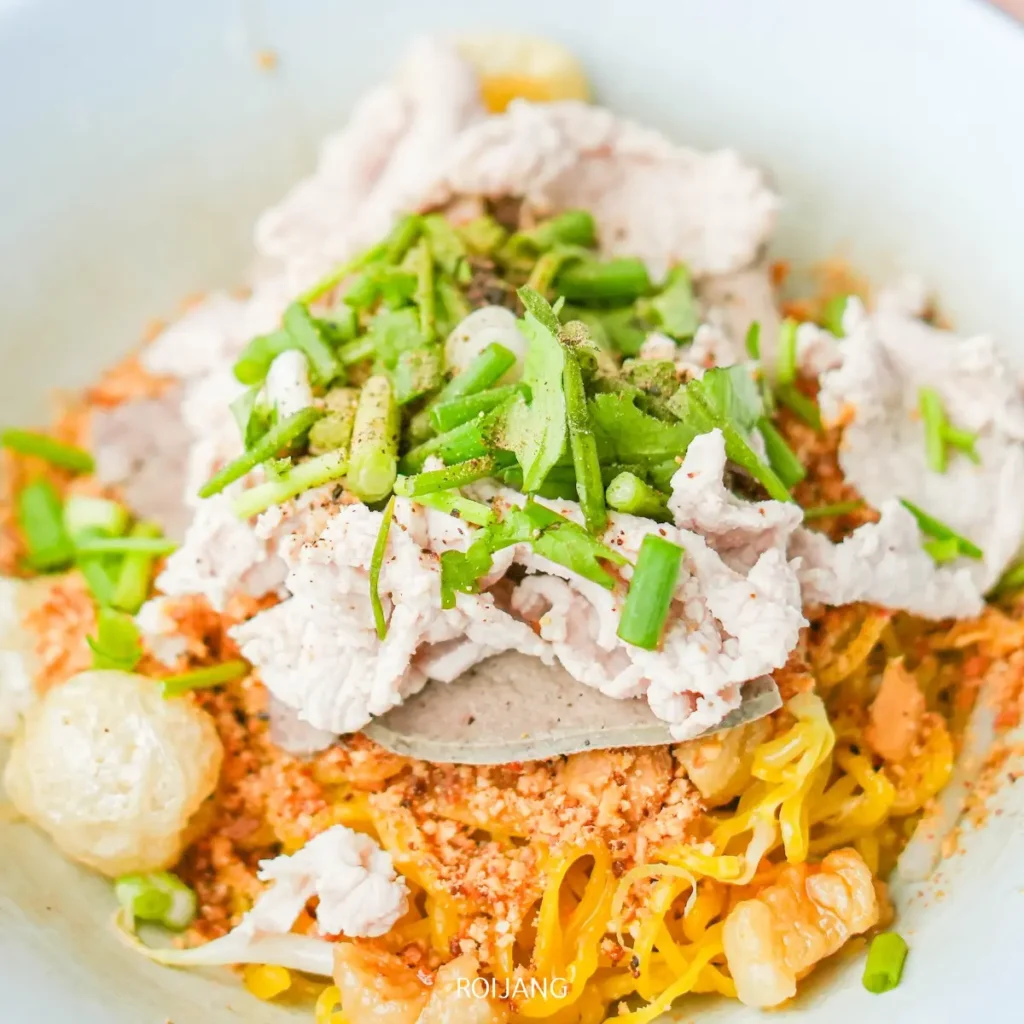 ชามบะหมี่ไข่สีเหลืองที่รู้จักกันในชื่อ ก๋วยเตี๋ยวเทวดา โรยหน้าด้วยเนื้อหมูต้มหั่นเป็นชิ้น ต้นหอมซอย และถั่วลิสงบด.