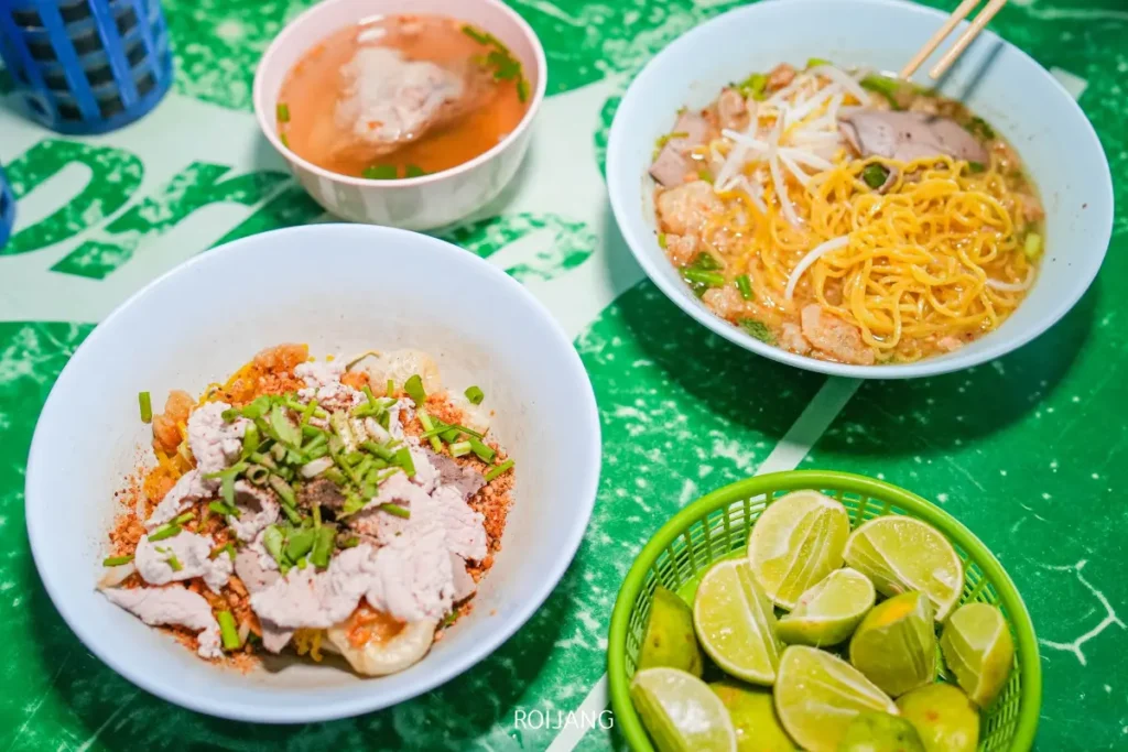 บะหมี่เวียดนามสามชามและก๋วยเตี๋ยวเทวดาพร้อมเนื้อสไลซ์และสมุนไพร เสิร์ฟพร้อมตะกร้าใส่มะนาว บนโต๊ะสีเขียว.