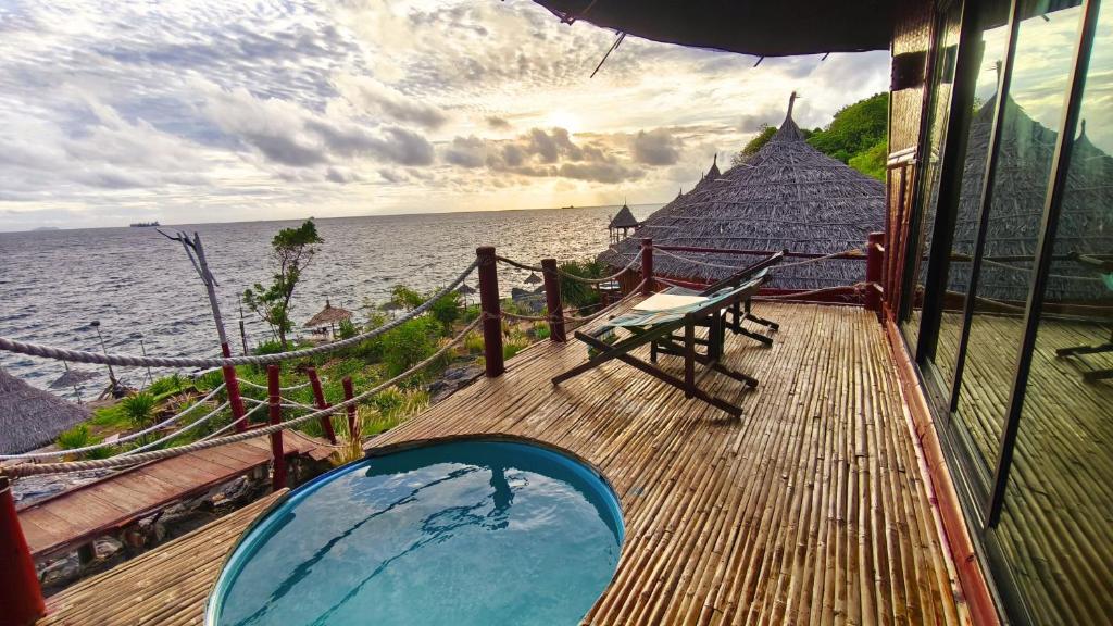 ระเบียงไม้พร้อมสระว่ายน้ำทรงกลมขนาดเล็กและเก้าอี้อาบแดดตั้งอยู่รวม ที่เที่ยวเกาะสีชัง เกาะสวยๆ ในที่เที่ยวชลบุรี ไป เที่ยวเกาะสีชัง เดินทางง่ายๆ ใกล้กรุงเทพแบบไปเช้าเย็นกลับได้ หลีกหนีความวุ่นวาย พร้อมอวดสถานที่สโลว์ไลฟ์
เหนือมหาสมุทรที่ ที่เที่ยวเกาะสีชัง โดยมีกระท่อมหลังคามุงจากและพืชพรรณเขียวขจีอยู่ใกล้ๆ ภายใต้ท้องฟ้าที่มีเมฆปกคลุม.