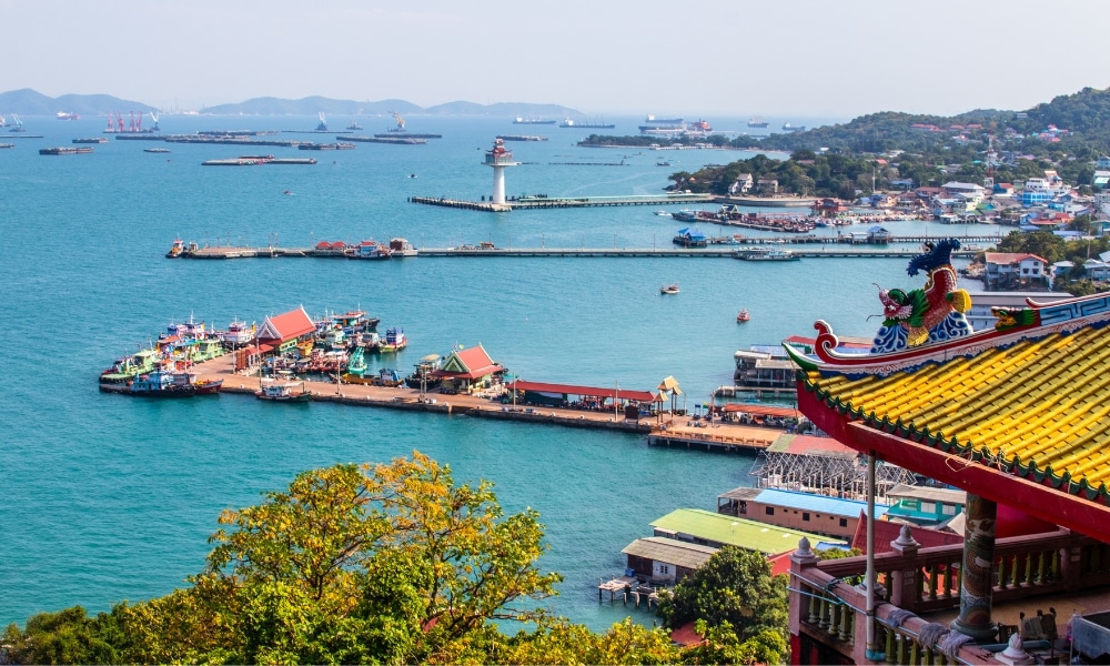 ภาพท่าเรือชายฝั่งที่มีเรือจอดอยู่ รวม ที่เที่ยวเกาะสีชัง เกาะสวยๆ ในที่เที่ยวชลบุรี ไป เที่ยวเกาะสีชัง เดินทางง่ายๆ ใกล้กรุงเทพแบบไปเช้าเย็นกลับได้ หลีกหนีความวุ่นวาย พร้อมอวดสถานที่สโลว์ไลฟ์
หลังคาสีสันสดใส ประภาคาร และเรือที่แล่นอยู่ไกลๆ มองจากตำแหน่งที่สูงขึ้นพร้อมสถาปัตยกรรมวัดที่ประดับประดาอย่างวิจิตรในเบื้องหน้า—เหมาะสำหรับผู้ที่มองหาสถานที่ท่องเที่ยวเกาะสีชัง.