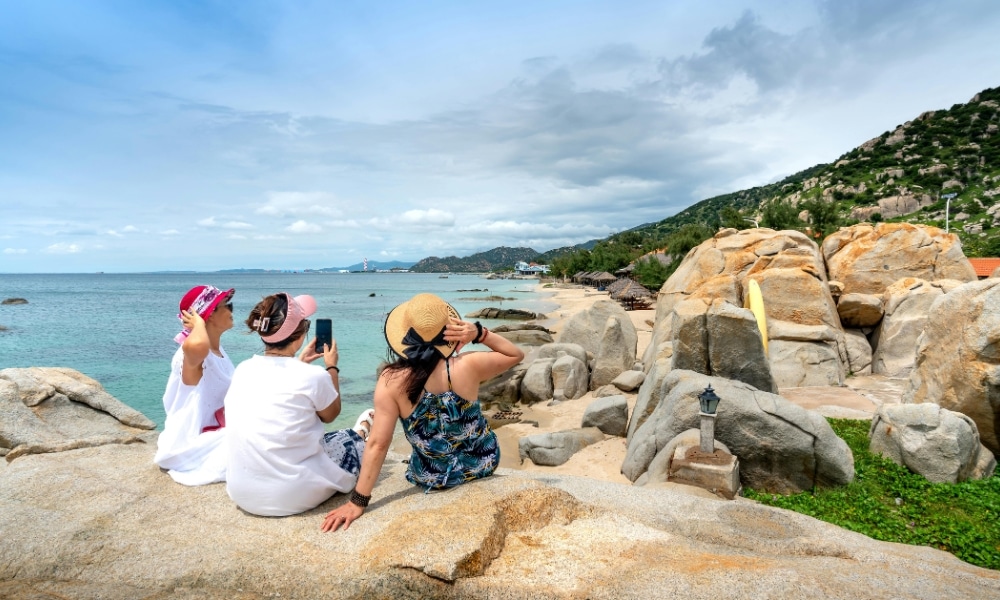 ผู้หญิงสามคนนั่งอยู่บนก้อนหินริมรวม ที่เที่ยวเกาะสีชัง เกาะสวยๆ ในที่เที่ยวชลบุรี ไป เที่ยวเกาะสีชัง เดินทางง่ายๆ ใกล้กรุงเทพแบบไปเช้าเย็นกลับได้ หลีกหนีความวุ่นวาย พร้อมอวดสถานที่สโลว์ไลฟ์
ทะเลที่เกาะสีชัง หันหลังให้กล้อง ขณะที่คนหนึ่งกำลังบันทึกช่วงเวลาด้วยโทรศัพท์มือถือของเธอ ภูเขาและท้องฟ้าที่มีเมฆครึ้มสร้างบรรยากาศที่สงบเงียบเป็นฉากหลัง.