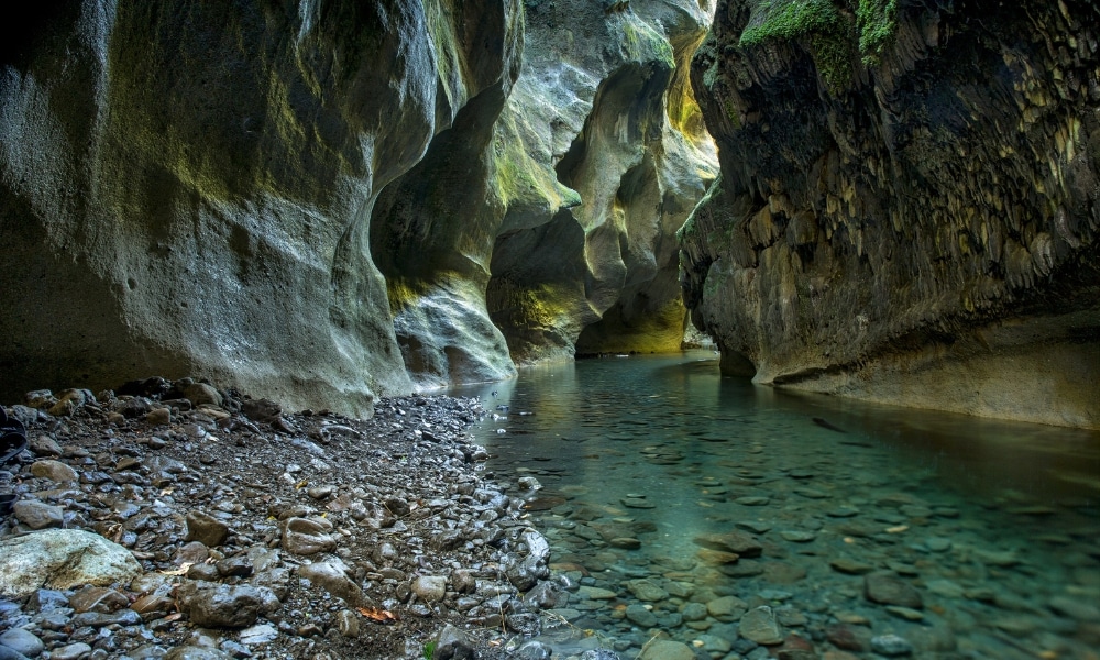 หุบเขาแคบที่มีหน้าผาหินสูงชัน มีมอสปกคลุมเป็นหย่อม ๆ และน้ำใสไหลผ่านก้อนหินเรียบไปตามชายฝั่งหิน—เป็น ที่เที่ยวชุมพร สถานที่ลับที่เหมาะสำหรับผู้ที่มองหา ชุมพรที่เที่ยว.