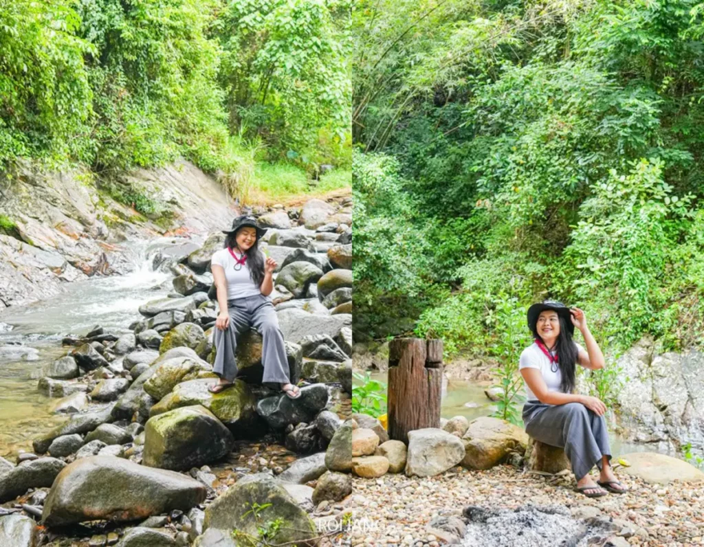 ผู้หญิงคนหนึ่งสวมหมวกและเสื้อผ้าลำลองนั่งอยู่บนก้อนหินริมลำธารในป่าเขียวชอุ่ม สัมผัสความเงียบสงบของซีแลนด์แอดเวนเจอร์ พังงา.