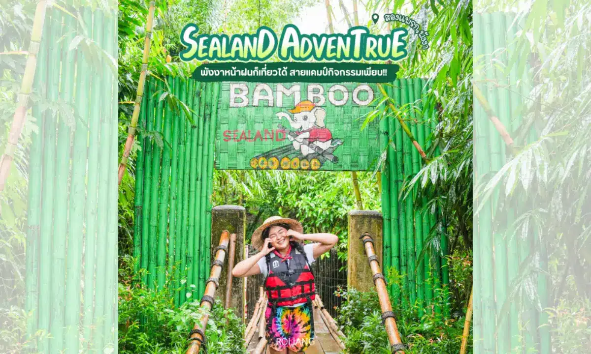 บุคคลที่สวมชุดสำหรับกิจกรรมกลางแจ้งโพสท่าและยิ้มอยู่หน้าป้ายทางเข้าธีมไม้ไผ่สีเขียวที่เขียนว่า "BAMBOO SEALAND" ที่ซีแลนด์แอดเวนเจอร์ พังงา.