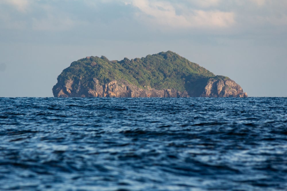 เกาะที่ห่างไกล ประกอบด้วยหินและป่าไม้ โผล่ขึ้นเหนือมหาสมุทรสีครามภายใต้ท้องฟ้าที่มีเมฆบางส่วน— ที่เที่ยวชุมพร เหมาะสำหรับทุกคนที่กำลังมองหาสถานที่ท่องเที่ยวในชุมพร หรือฝันถึงประสบการณ์การท่องเที่ยวในชุมพรที่ไม่เหมือนใคร.