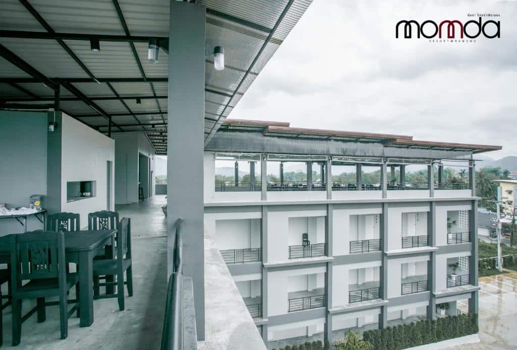 ทางเดินและพื้นที่นั่งเล่นกลางแจ้งมองเห็นอาคารหลายชั้นสมัยใหม่พร้อมระเบียงภายใต้ท้องฟ้าที่มีเมฆครึ้ม เหมาะสำหรับผู้ที่มองหา ที่พักระนอง โรงแรมระนองหรือที่พักระนองในเมืองสำหรับการพักผ่อนอย่างสบาย.
