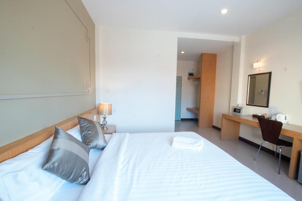 ห้องพักที่เรียบร้อยใน โรงแรมระนอง  พร้อมเตียงที่จัดไว้อย่างเรียบร้อย หมอน โคมไฟข้างเตียง โต๊ะพร้อมเก้าอี้ กระจกติดผนัง และอุปกรณ์ชงชา.