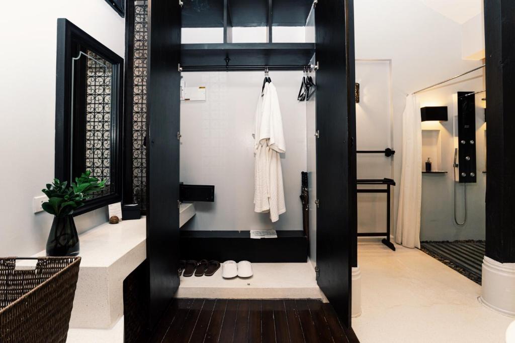 ห้องน้ำสมัยใหม่ที่ โรงแรมระนอง  ประกอบด้วยตู้เสื้อผ้าสีดำแบบเปิดโล่งพร้อมเสื้อคลุม แขวนเสื้อผ้า รองเท้าแตะ โต๊ะเครื่องแป้งพร้อมกระจก ต้นไม้ใหญ่ และห้องอาบน้ำแบบวอล์กอินอยู่ด้านหลังเพื่อการผ่อนคลายอย่างเต็มที่.