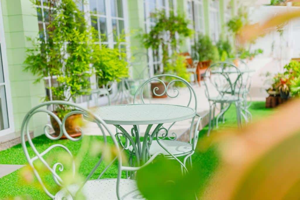 ชุดโต๊ะและเก้าอี้สนามหญ้าเทียมสำหรับกลางแจ้ง พร้อมต้นไม้ใน ที่พักระนอง กระถางและหน้าต่างบานใหญ่เป็นฉากหลัง—เหมาะสำหรับการพักผ่อนอย่างสบายที่ ที่พักระนอง ที่ทันสมัย หลังจากสำรวจทิวทัศน์ที่สวยงามของ โรงแรมระนอง.