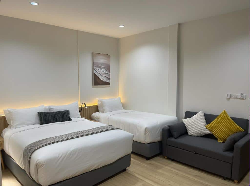 ห้องพักโรงแรมพร้อมเตียงคู่, เตียงเดี่ยว, โซฟาสีเทาพร้อมหมอนอิง, พื้นไม้สีอ่อน, และภาพติดกรอบบนผนัง ที่พักระนอง เหมาะสำหรับการเข้าพักของคุณที่ โรงแรมระนอง.