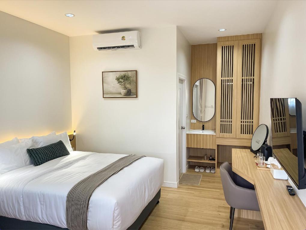 ห้องพักโรงแรมระนองสไตล์โมเดิร์น พร้อมเตียงคู่ โต๊ะทำงาน โทรทัศน์ ตู้เสื้อผ้า พื้นที่แต่งตัวพร้อมกระจก  ที่พักระนอง และเครื่องปรับอากาศติดผนัง การตกแต่งภายในเน้นความเรียบง่าย ใช้ไม้สีอ่อนและโทนสีธรรมชาติเพื่อความผ่อนคลายระหว่างการเข้าพัก.