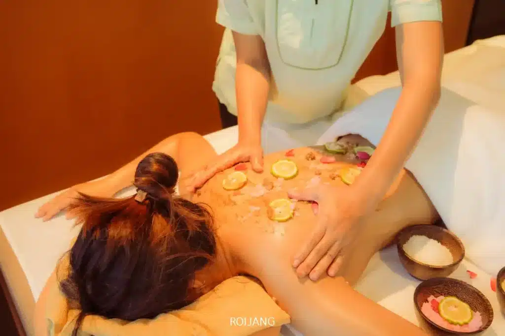 ที่ราตนา สปา ผู้มาเยือนจะได้รับการนวดผ่อนคลายบริเวณหลังด้วยมะนาวฝานและกลีบดอกไม้บนแผ่นหลัง พร้อมบรรยากาศล้อมรอบด้วยชามเกลือและส่วนผสมจากธรรมชาติ.