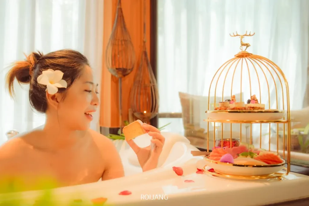 ที่ราตนา สปา หญิงสาวในอ่างอาบน้ำถือขนมปังและจ้องมองไปที่ชั้นวางของสีทองที่มีของว่างหลากหลายชนิดอยู่ข้างๆเธอ.