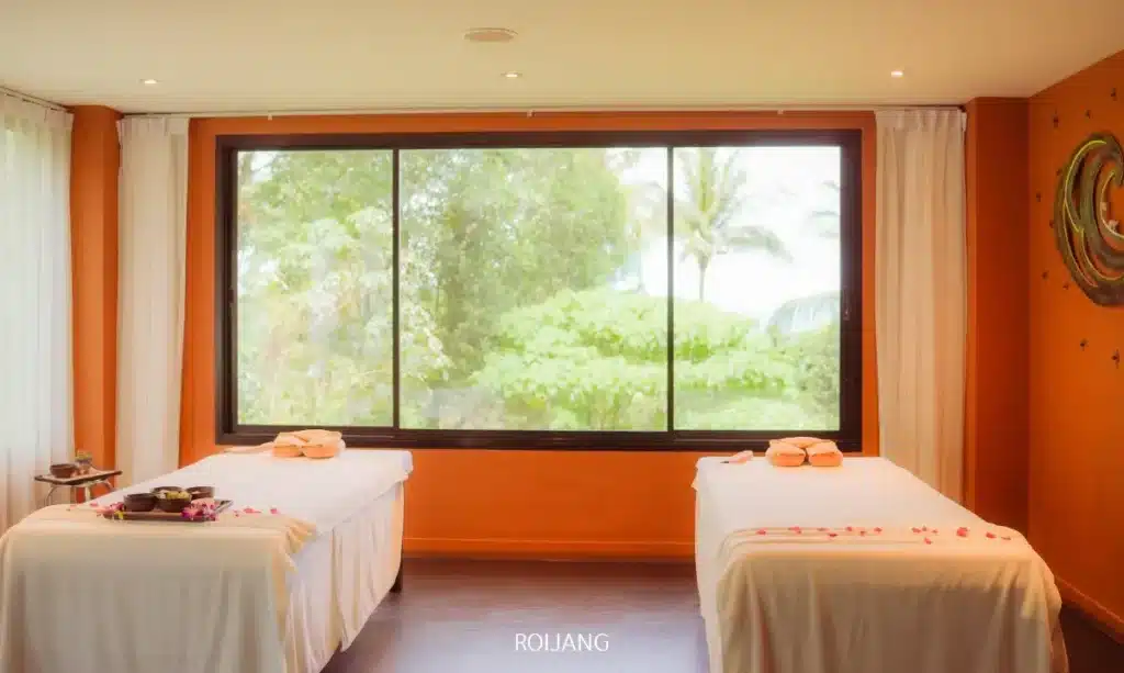 ห้องนวดที่เงียบสงบที่ราตนา สปา มีเตียงนวดสองเตียงที่เตรียมไว้อย่างดี ผ้าขนหนูเนื้อนุ่ม และอุปกรณ์สปาหรูหราใกล้หน้าต่างบานใหญ่ที่มองเห็นวิวสีเขียวชอุ่ม.