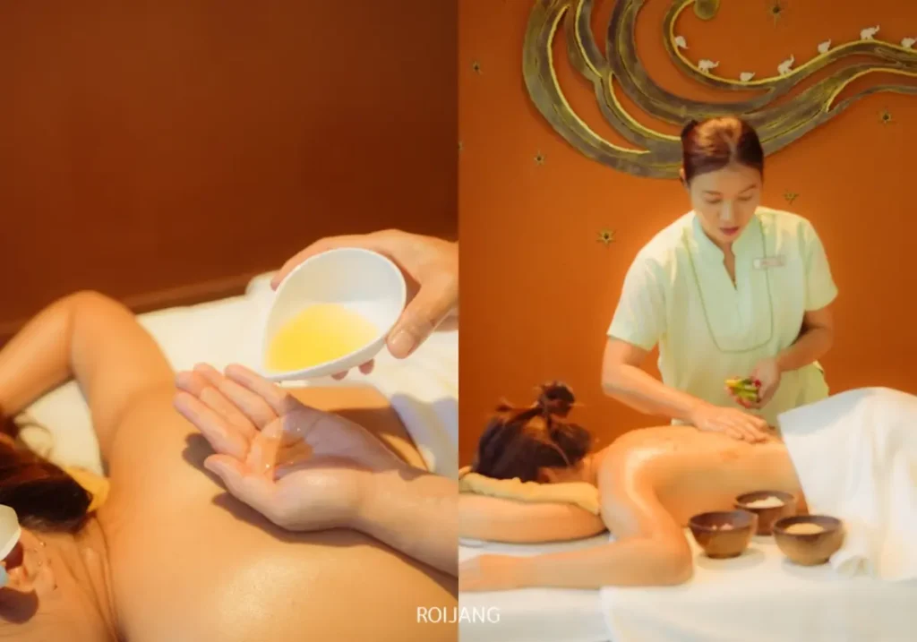 บุคคลหนึ่งนอนคว่ำหน้าลงบนเตียงนวดที่ร้านนวด Ratana Spa โดยได้รับการนวดน้ำมันอุ่นที่ถูกลงบนหลังและนวดผ่อนคลายจากนักบำบัดนวดในบรรยากาศที่มีแสงไฟนุ่มนวล.