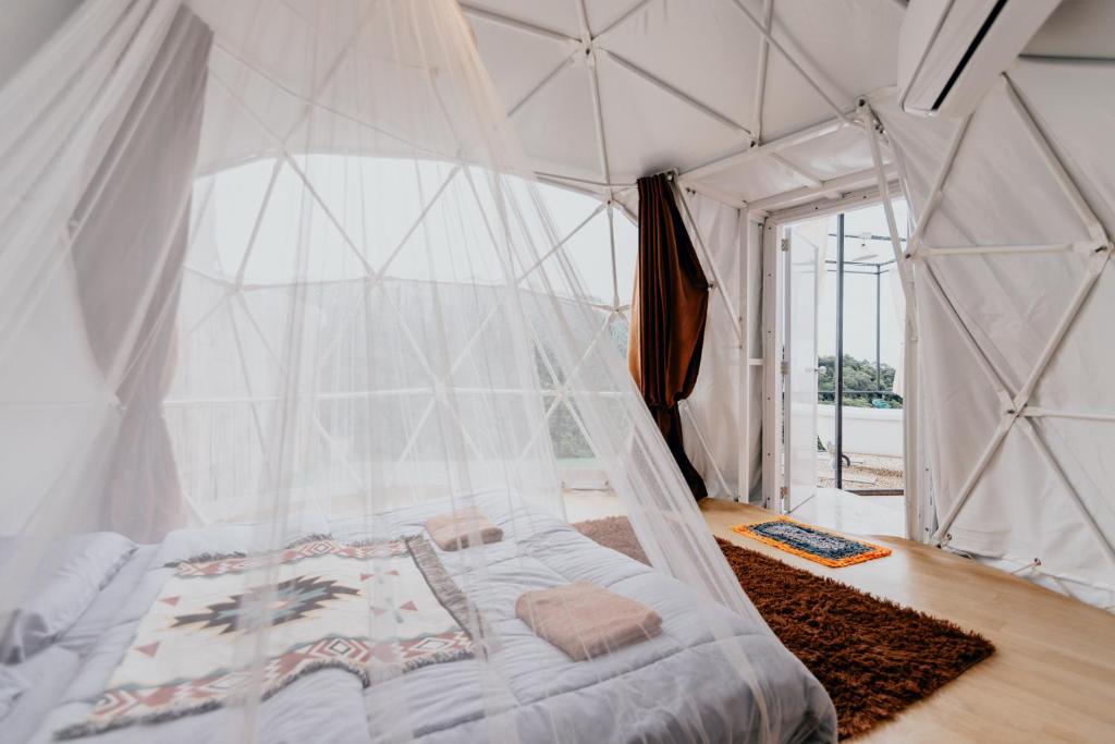 ห้องนอนโดมทรงจีโอเดสิกพร้อมเตียงที่คลุมด้วยมุ้งสีขาว ผ้าห่มลายสวย ประตูเปิดโล่ง และวิวต้นไม้สีเขียวด้านนอก—รีสอร์ทเชียงใหม่สุดพิเศษที่โอบล้อมด้วยธรรมชาติ.
