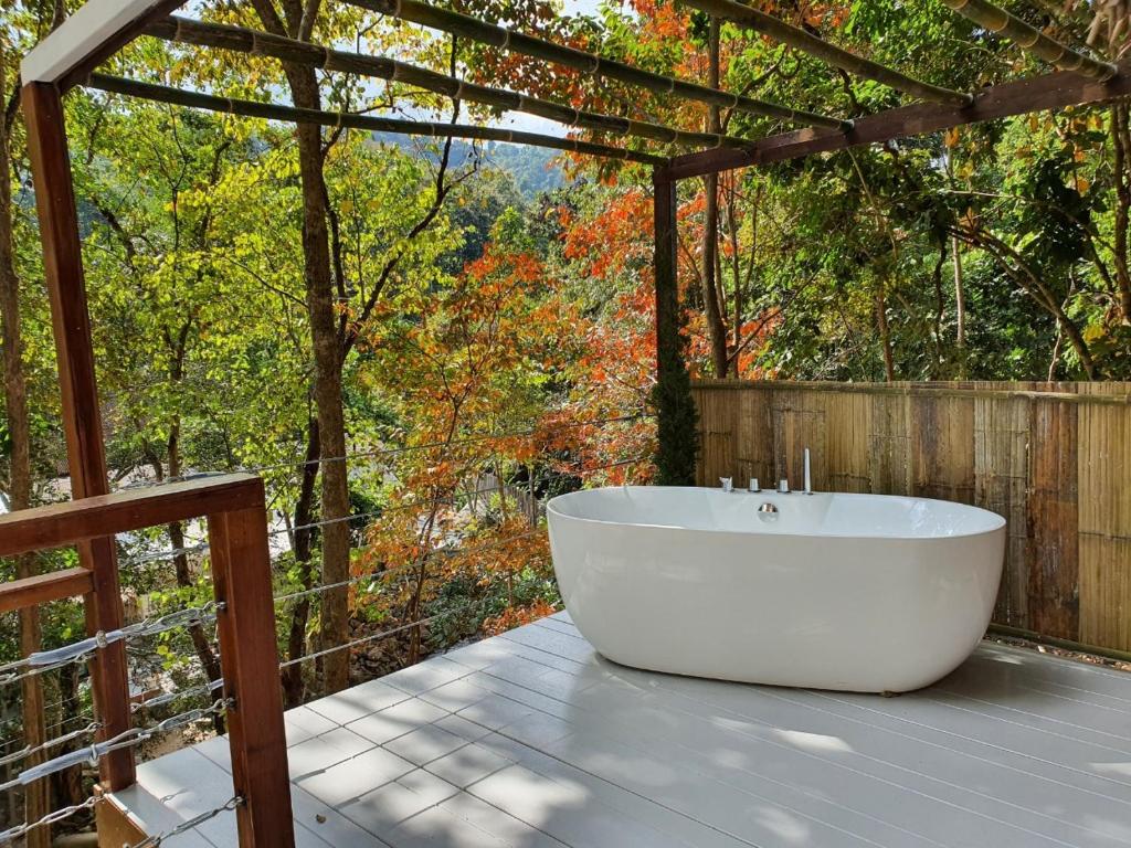 อ่างอาบน้ำสีขาวตั้งอยู่กลางลานไม้ที่มีซุ้มไม้ระแนบล้อมรอบด้วยต้นไม้ที่มีใบสีเขียวและส้ม—ภาพที่ชวนให้หลงใหลซึ่งมักพบได้ที่รีสอร์ทเชียงใหม่ที่เงียบสงบ.