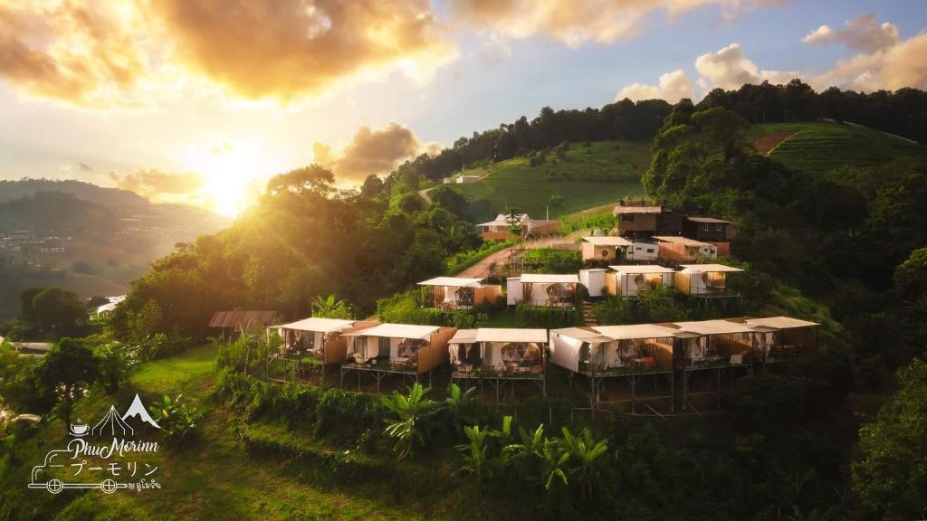 รีสอร์ทบนเนินเขาเชียงใหม่ที่มีเต็นท์สีขาวและอาคารขนาดเล็กซ่อนตัวอยู่ในความเขียวขจี ถ่ายภาพในยามพระอาทิตย์ตกดินขณะที่แสงอาทิตย์ส่องผ่านเมฆ.
