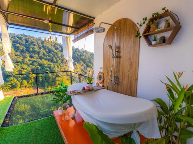 บรรยากาศสปากลางแจ้งที่รีสอร์ทเชียงใหม่ประกอบด้วยเตียงนวด, ห้องอาบน้ำ, ต้นไม้ในกระถางที่เขียวชอุ่ม, และวิวทิวทัศน์ของภูเขาเขียวขจีเป็นฉากหลัง.