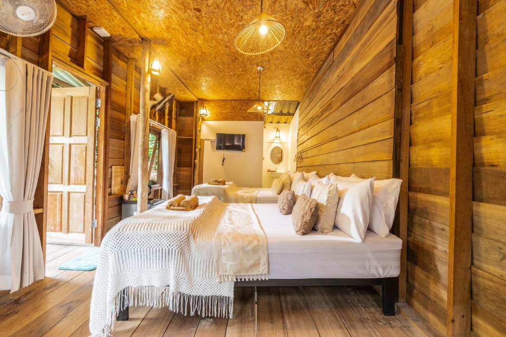 ห้องนอนที่อบอุ่นในโรงแรมเชียงใหม่ที่มีผนังและเพดานไม้ เตียงสองเตียงที่จัดไว้อย่างเรียบร้อยพร้อมผ้าปูที่นอนสีขาว โทรทัศน์ติดผนัง และประตูเปิดรับแสงธรรมชาติ.