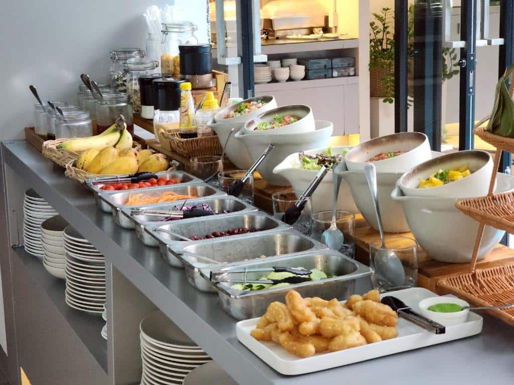 โต๊ะบุฟเฟ่ต์ที่เต็มไปด้วยสลัดสด ผลไม้ น้ำสลัด และอาหารทอด ถูกจัดเรียงอย่างเรียบร้อยในพื้นที่รับประทานอาหารที่สว่างสดใสที่ โรงแรมเชียงใหม่ มอบประสบการณ์การรับประทานอาหารที่น่าประทับใจให้แก่แขกผู้เข้าพัก.