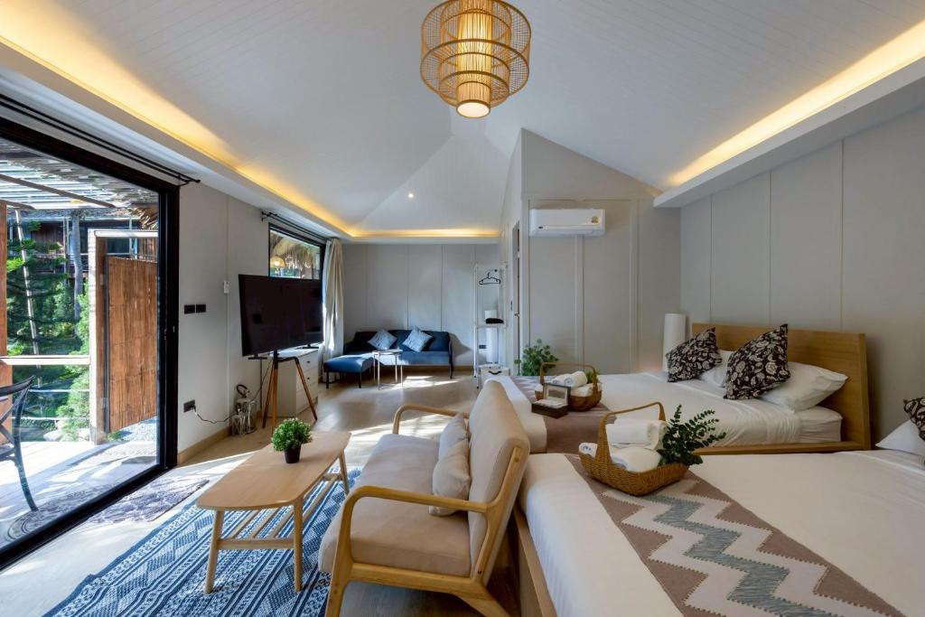 ห้องพักโรงแรมสมัยใหม่ในโรงแรมที่เชียงใหม่ มีเตียงสองเตียง, โซฟา, ทีวี, โต๊ะกาแฟ, และประตูบานเลื่อนกระจกขนาดใหญ่เปิดไปยังระเบียงที่มีที่นั่งกลางแจ้ง.