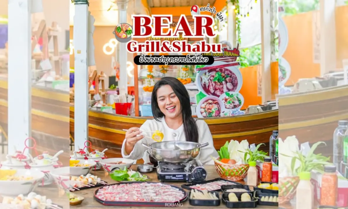 บุคคลหนึ่งนั่งอยู่ที่โต๊ะพร้อมด้วยวัตถุดิบสำหรับชาบูชาบูและปิ้งย่างหลากหลายชนิด ยิ้มและกำลังปรุงอาหารที่ร้าน Bear Grill & Shabu.