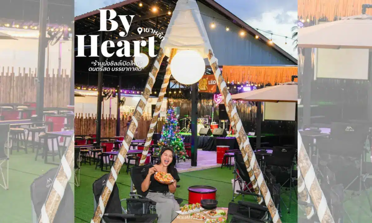 ผู้หญิงคนหนึ่งนั่งอยู่ภายในเต็นท์ที่ตั้งอยู่ในร้านอาหารกลางแจ้ง ถือพิซซ่าไว้ในมือ บริเวณนั้นประดับด้วยไฟ โต๊ะ และต้นคริสต์มาส—ถ่ายทอดบรรยากาศอบอุ่นของเทศกาลวันหยุดได้อย่างเต็มเปี่ยม.