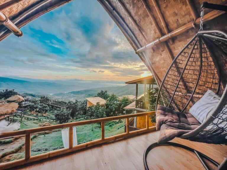 ห้องไม้ไผ่และไม้สักพร้อมเก้าอี้หวายแขวนที่มองเห็นวิวหุบเขาและภูเขาที่สวยงามในยามพระอาทิตย์ขึ้นหรือพระอาทิตย์ตก มอบทัศนียภาพของต้นไม้เขียวขจีและท้องฟ้าสดใส—ที่พักเชียงใหม่ในอุดมคติสำหรับผู้รักธรรมชาติที่ต้องการความสงบเงียบ.