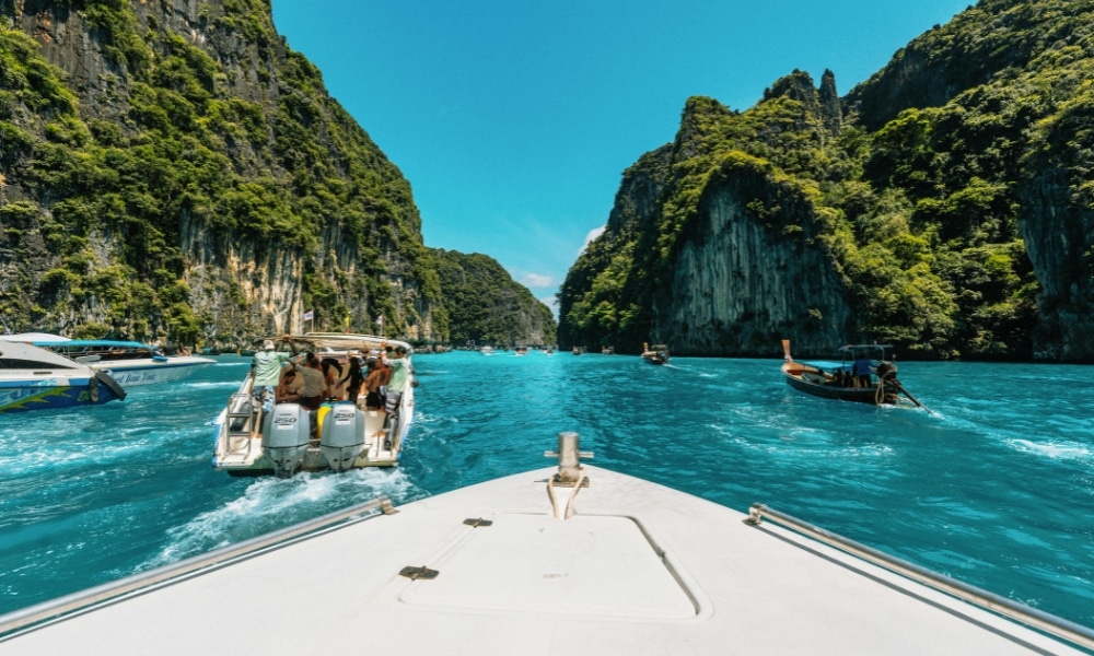 วิวจากเรือที่ล่องผ่านน้ำใสสีฟ้า ท่ามกลางหน้าผาหินปูนสีเขียวและเรือลำอื่น ๆ ที่อยู่ข้างหน้าในทะเลสาบน้ำเค็มเขตร้อน—เหมาะสำหรับผู้ที่ต้องการสถานที่ท่องเที่ยวธรรมชาติใกล้กรุงเทพฯ สำหรับการหนีไปพักผ่อนอย่างรวดเร็ว.